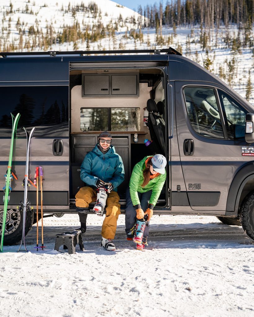 A couple sitting in their camper van putting their winter ski boots on.